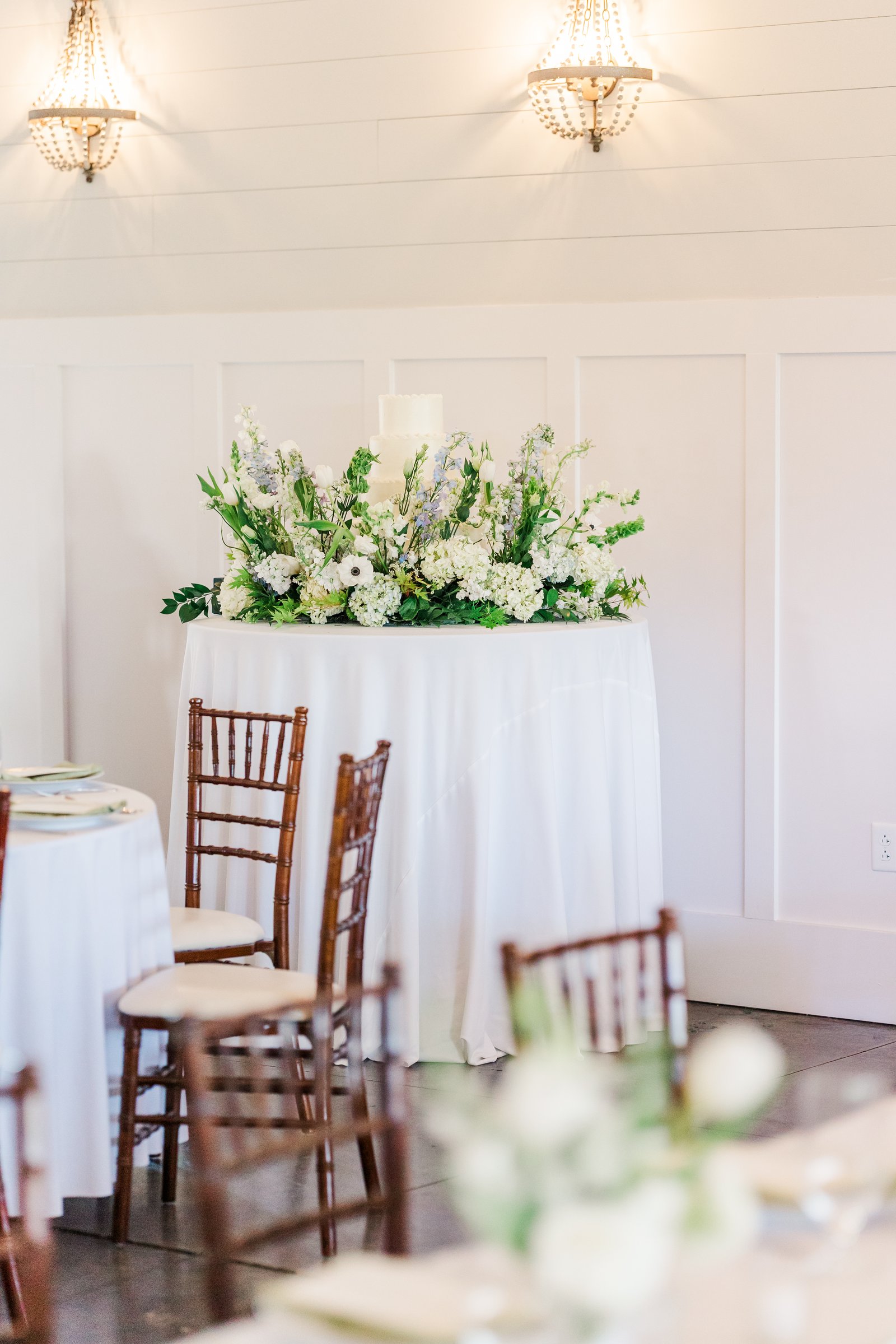 Wedding cake on a table with a lush white floral meadow arrangement